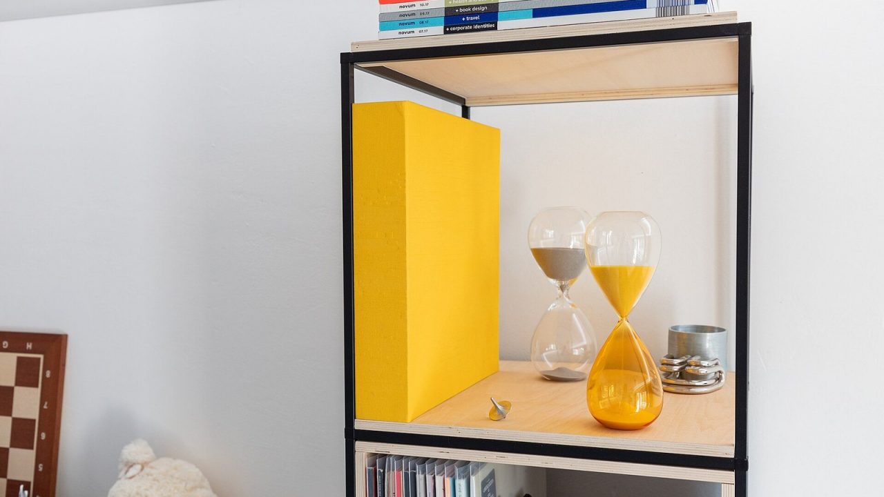 Two decorative hourglasses with yellow and grey sand on a bookshelf